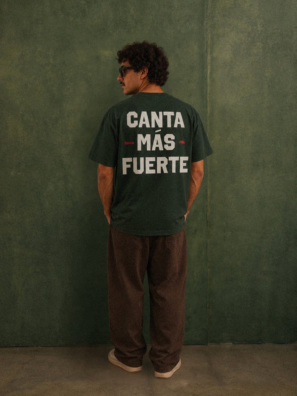 Mexico Azteca 12 tee, forest green, man wearing oversized fit showing Canta Más Fuerte back print, studio shot