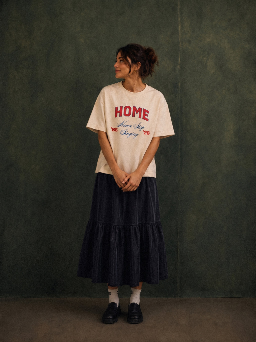 Home tee, cream, woman wearing oversized boxy fit showing HOME Never Stop Singing 66 26 front print, green studio shot