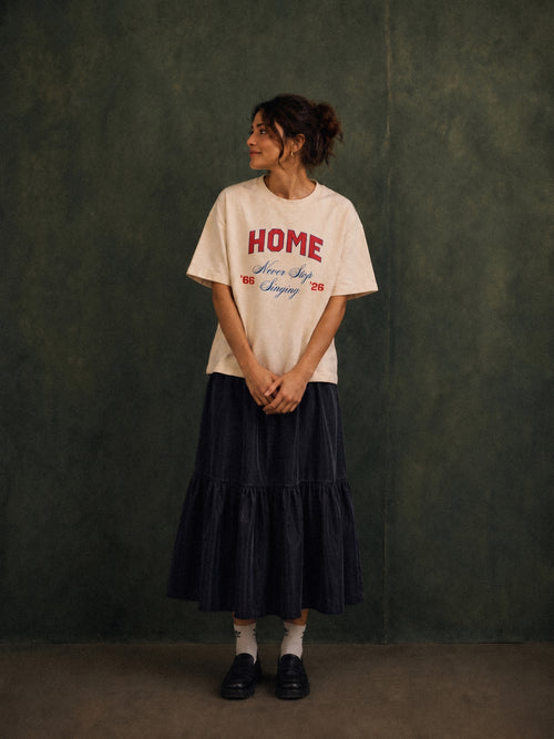 Home tee, cream, woman wearing oversized boxy fit showing HOME Never Stop Singing 66 26 front print, green studio shot