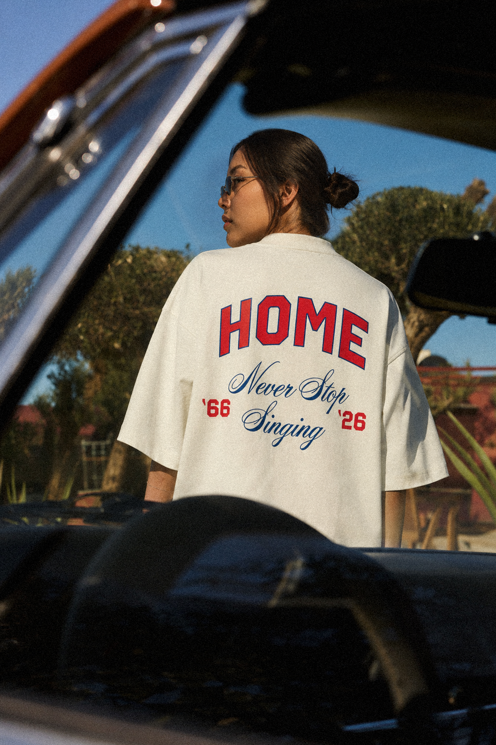 It's Coming tee, cream, woman wearing oversized boxy fit showing HOME Never Stop Singing back print, outdoor vintage car lifestyle shot