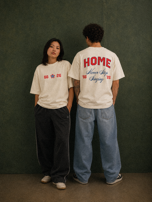 It's Coming tee, cream, man and woman wearing oversized boxy fit showing 66 Three Lions 26 front print and HOME Never Stop Singing back print, green studio lifestyle shot