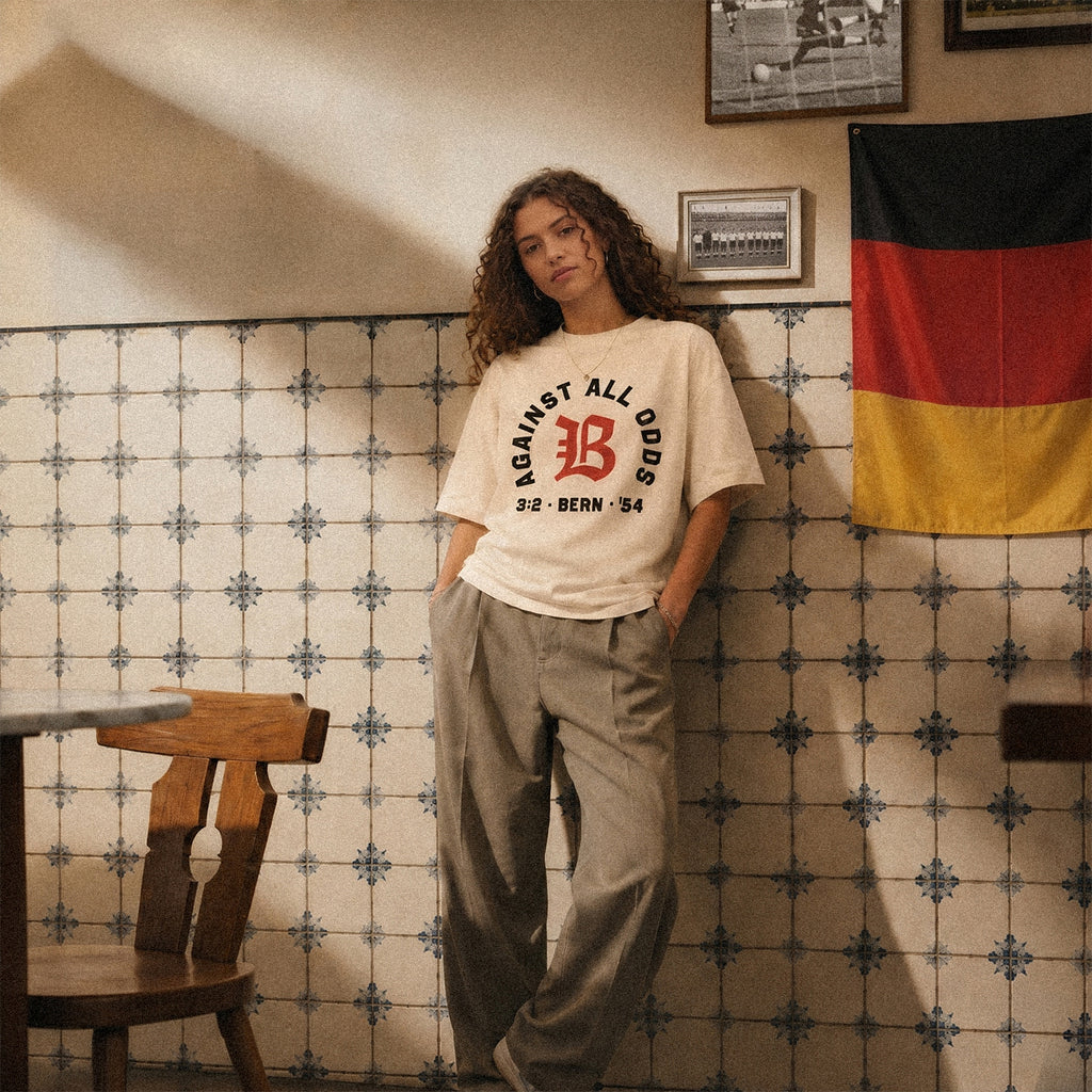 Nobody Believed tee, cream, woman wearing oversized boxy fit showing Against All Odds front print, indoor lifestyle shot with German flag