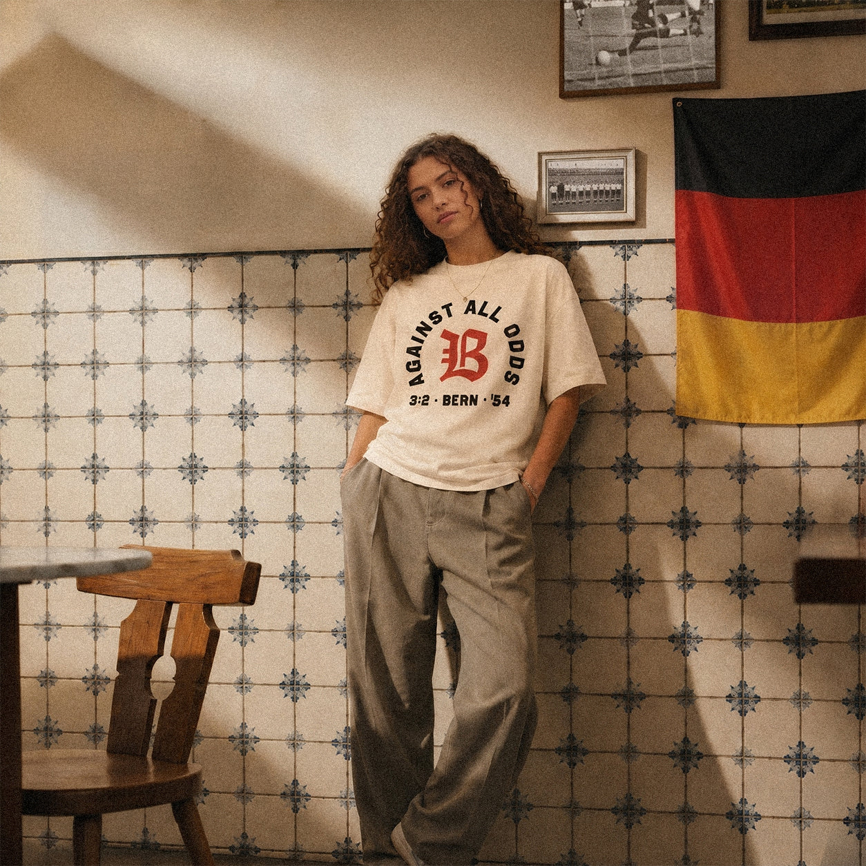 Nobody Believed tee, cream, woman wearing oversized boxy fit showing Against All Odds front print, indoor lifestyle shot with German flag