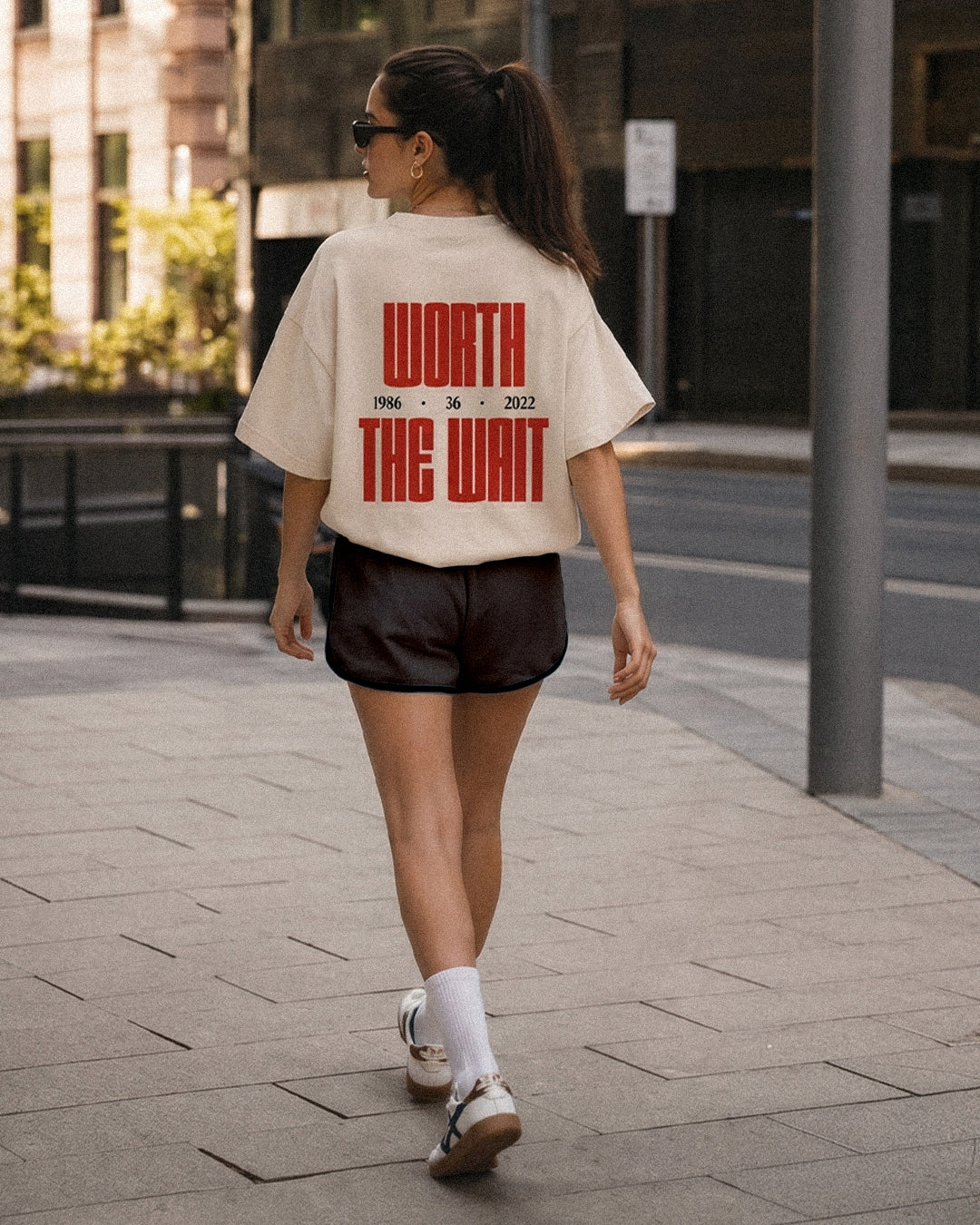 We Can tee, cream, woman wearing oversized boxy fit showing Worth The Wait back print, outdoor street lifestyle shot