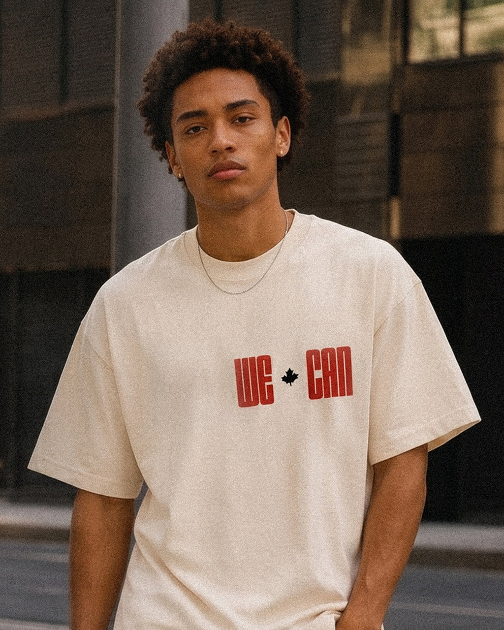 We Can tee, cream, man wearing oversized boxy fit showing We Can maple leaf front print, outdoor urban lifestyle shot