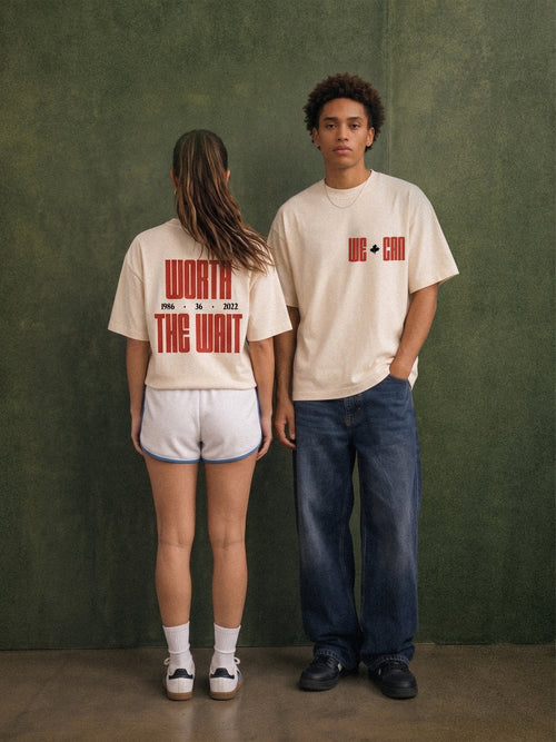 We Can tee, cream, man and woman wearing oversized boxy fit showing We Can front print and Worth The Wait back print, green studio lifestyle shot